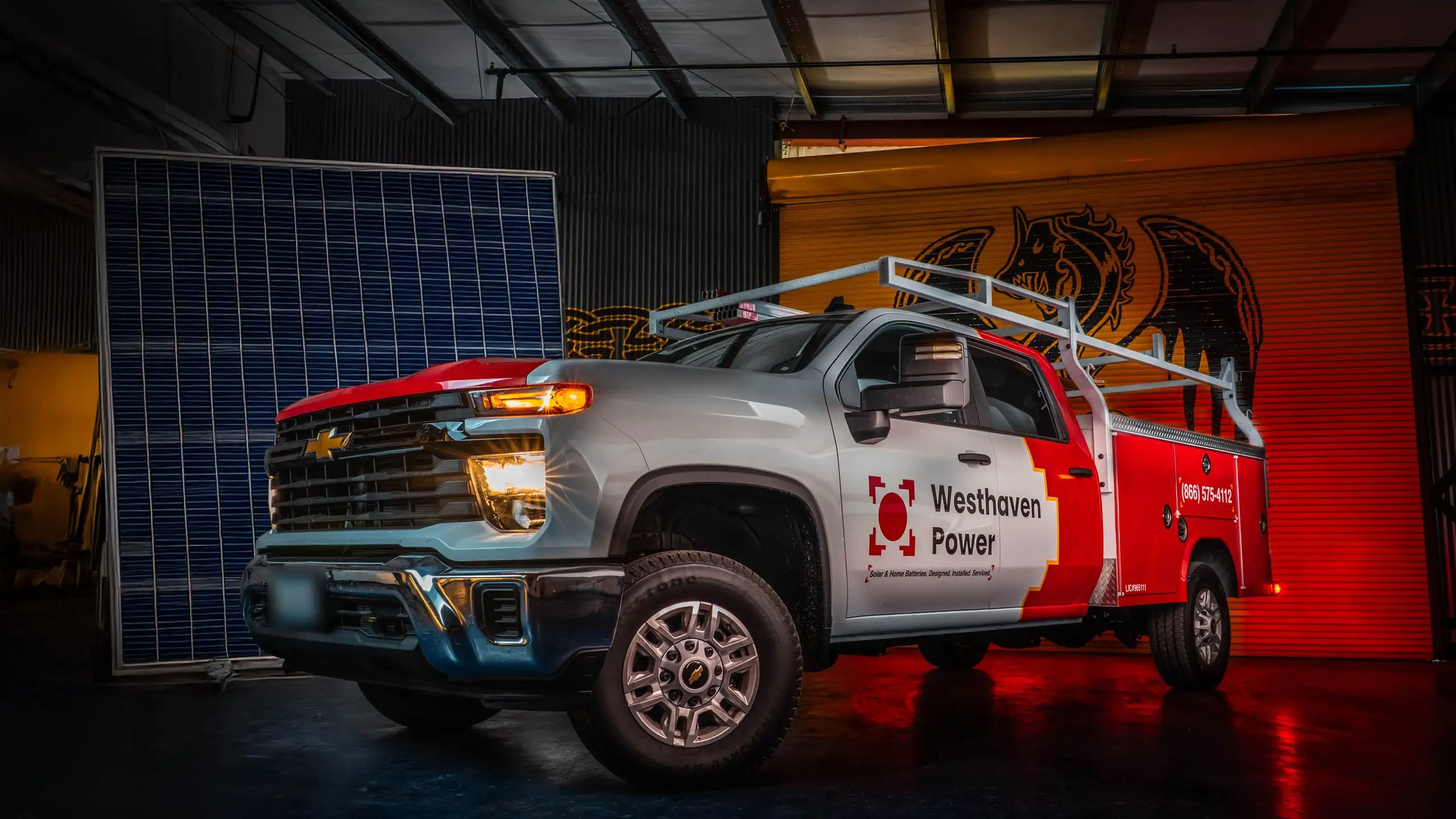 A wrapped Westhaven Power service truck parked in the warehouse beside a solar panel, lit like a portrait.