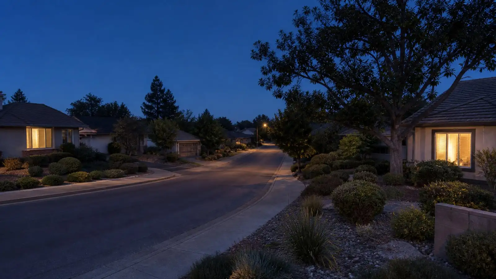 A quiet Northern California street at dusk with warm light in the windows.