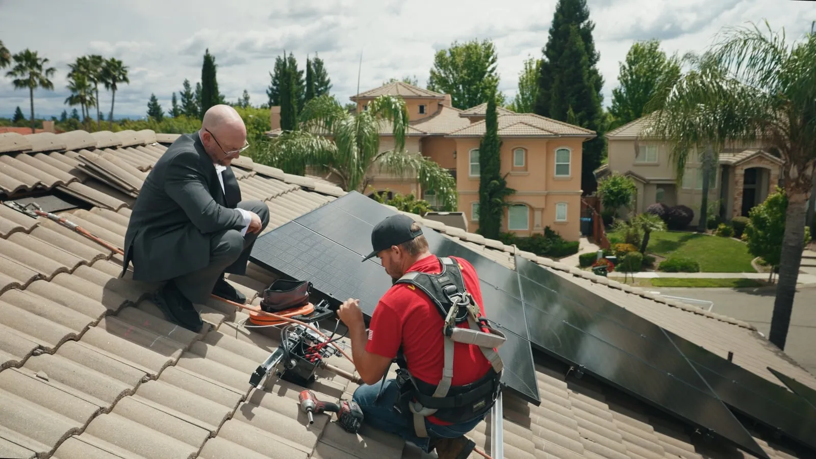 A harnessed Westhaven installer works at black solar panels on the tile roof of a Nor-Cal home while a consultant looks on.