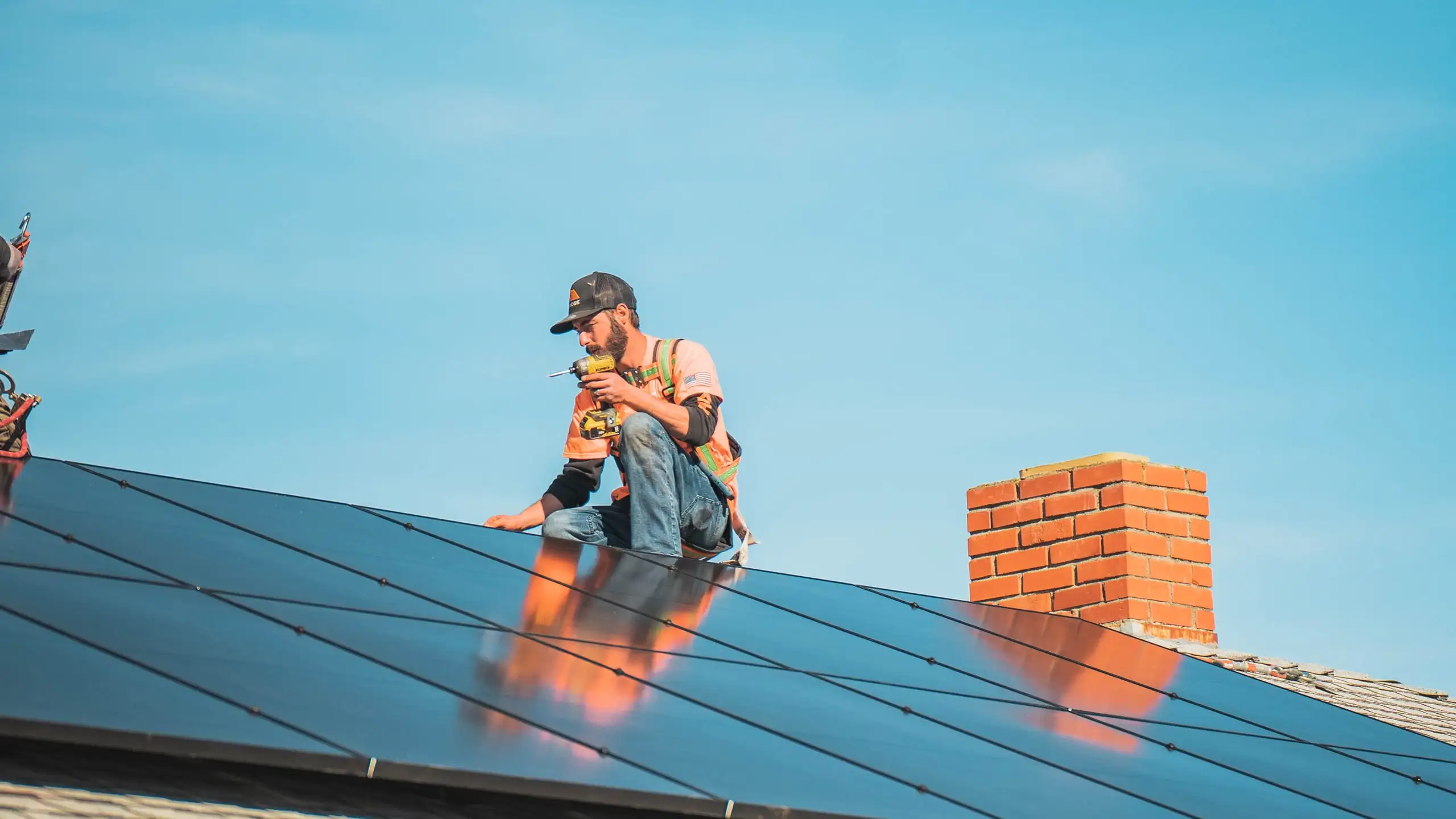 A harnessed Westhaven installer works on a black solar array beside a brick chimney under a blue sky.